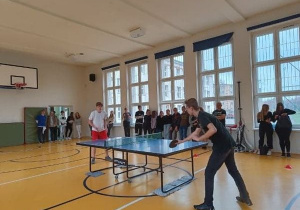 Uczniowie na sali gimnastycznej grają w tenisa stołowego.