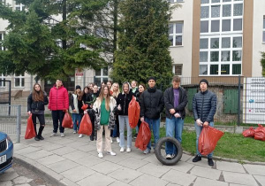 Uczniowie stoją przed budynkiem szkoły i eksponują zebrane worki śmieci.